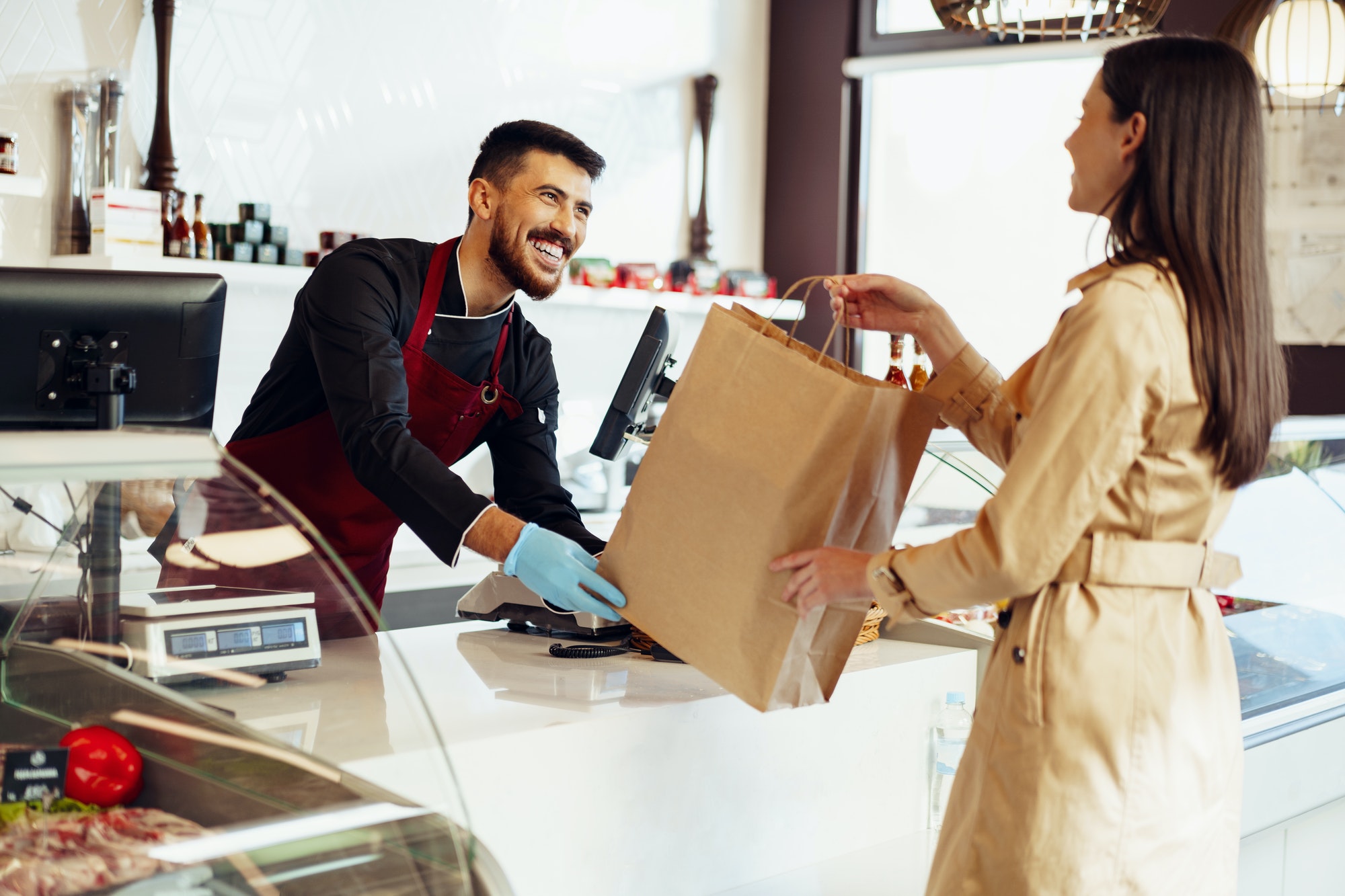 Shop assistant handling shopping bag to female customer in grocery store